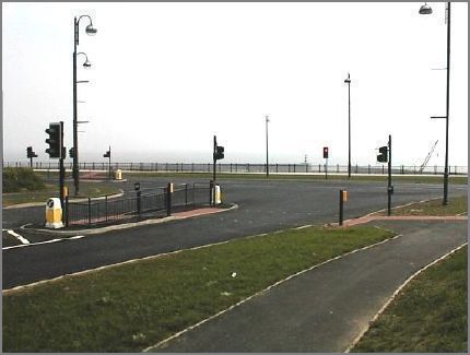 The fencing defines the boundary of the Harbour.  The lighthouse can just be seen in the distance. The George Elmy Lifeboat Way runs left to right across the picture.