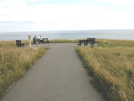 The tarmac walkway has finally brought us here. There is a plaque to verify our position.  The view looks eastwards  to the sea. Here you may sit and rest and enjoy the sunshine. Behind us to the west is the Noses Point Car Park and beyond that the road can be seen stretching away westwards.